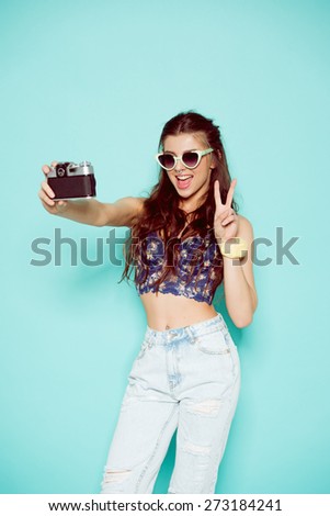 hipster photographer fashion stylish woman dancing and making photo using retro camera. Portrait on blue background in white sweater