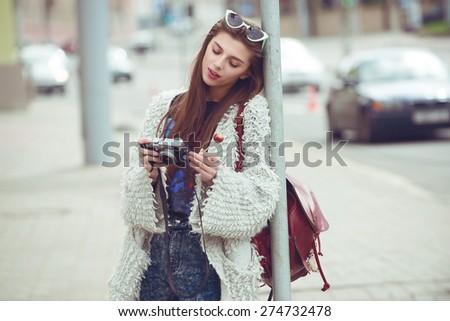 urban fashion woman tourist keep candy on a stick and digital compact camera and look photo on screen. Hipster style sunglasses and coat. street style outdoor portrait