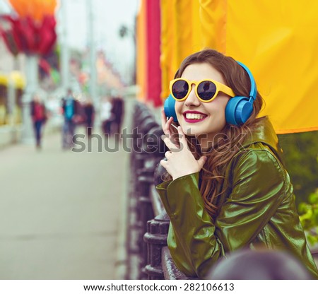 outdoor street style hipster dj woman in yellow sunglasses and dj headphones listen music and smile