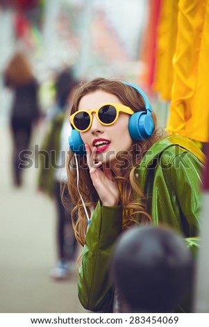 outdoor street style hipster dj woman in yellow sunglasses and dj headphones listen music and smile