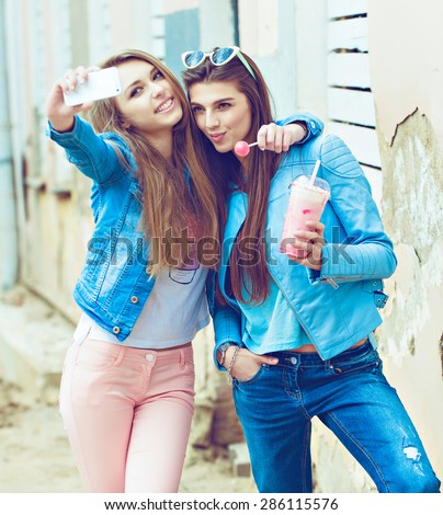 Hipster girlfriends taking a selfie in urban city context. Concept of friendship and fun with new trends and technology. Best friends eternalizing the moment with modern smartphone