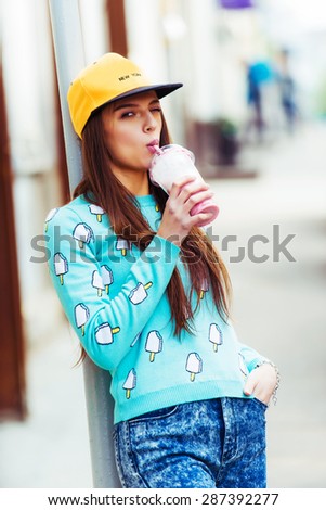 Fashion hipster girl with cup of sweet cocktail on city street