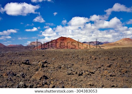 Field of lava volcanic bombs stones against the background of red volcano hill of Timanfaya National Park. Lanzarote, Canary Islands, Spain
