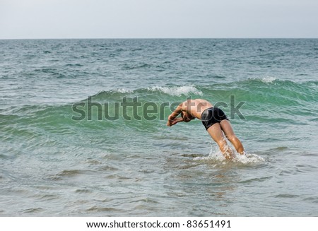 Young man duck diving a small ocean wave.