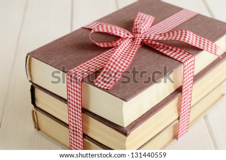 Book bundle bounded up in red-and-white ribbon on white wooden background