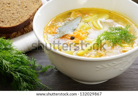 Homemade fish soup with potato, carrots, rice, pepper and bay leaf served with dark bread and dill on wooden background