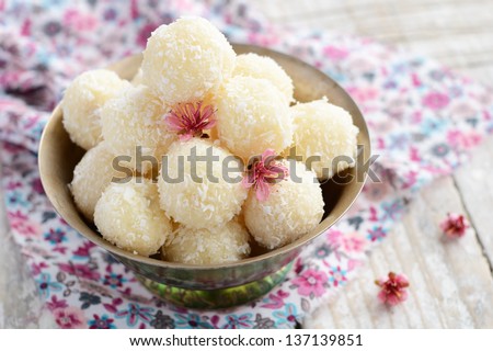 Homemade coconut balls decorated with little pink flowers in metal bowl, wooden background