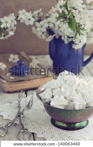 Still life in vintage style with meringue kisses and cherry flowers on rusted wooden table