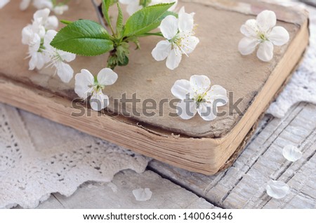 Decoration in vintage style with cherry flowers laying upon old book on lace doily