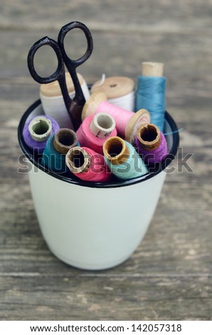 Set of colorful vintage thread spools in white bucket on rusted wooden background