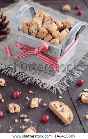 Cranberry biscotti in decorative crate on linen napkin on rusted wooden table with selective focus on bow