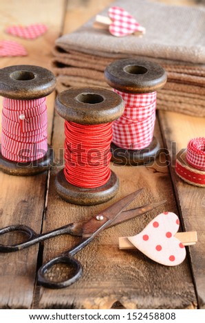 Decoration with vintage ribbon spools, burlap and red hearts on rusted wooden background
