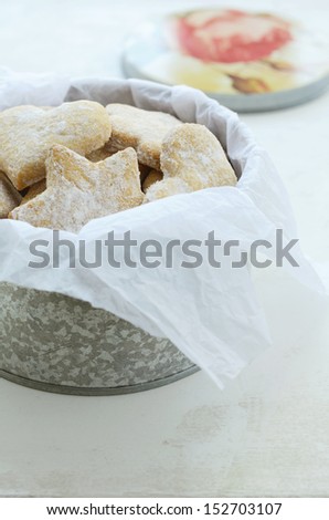 Star and heart shaped ginger cookies with sugar powder wrapped in parchment paper and placed in tin box, on light background