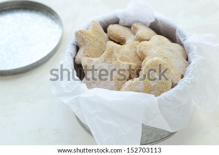 Star and heart shaped ginger cookies with sugar powder wrapped in parchment paper and placed in tin box, on light background
