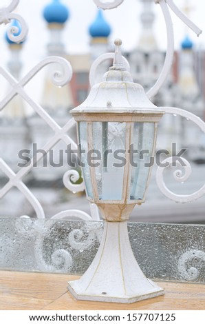 White outdoor lantern under the rain on a table in cafe with church view