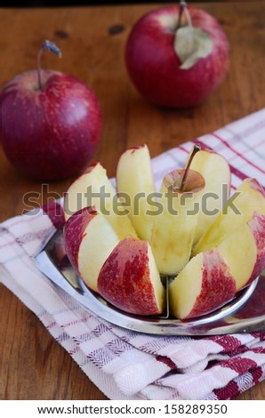 Ripe red apple with metal cutter on red and white kitchen towel on rusted wooden table