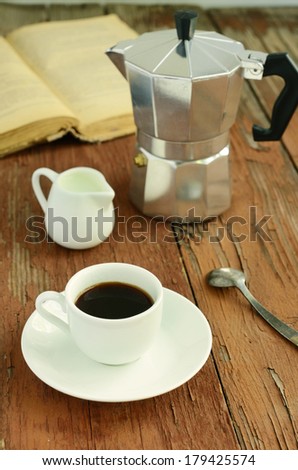 Cup of espresso,coffee pot, pitcher with milk and old book on rusted wooden table