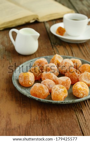 Dried sugared kumquats on rusted metal plate, milk pot, cup of coffee and old book on rusted wooden table
