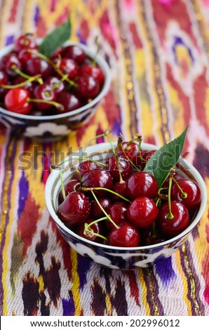 Ripe cherry in authentic uzbek tea bowls on bright ethnic fabric