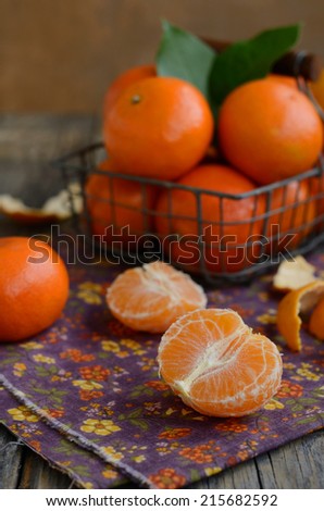 Cloves of tangerines and wire basket full of ripe fruits against wooden background with copyspace