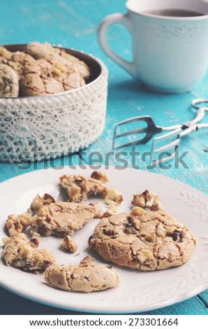 Homemade almond cookies with walnut on white plate  and cup of tea placed on blue shabby wooden background
