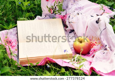 Picnic in summer garden - apple and open book over bright fabric