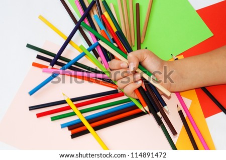 Child\'s hand with color pencils. Paper in more colors in the background.