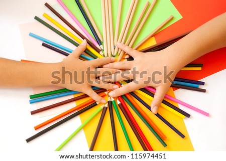 Wooden pencils and two children\'s hands from above. Paper in more colors in the background. Top view.
