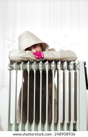 Freezing Young Girl in Winter Jacket Near a Heater.