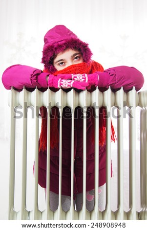Freezing Young Girl in Winter Jacket Near a Heater.