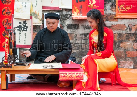 HANOI, VIETNAM, JANUARY 28: Old master write ancient letters for a girl in Aodai costume on January 28, 2014 in Hanoi, Vietnam. This is a tradition of vietnamese people in lunar new year