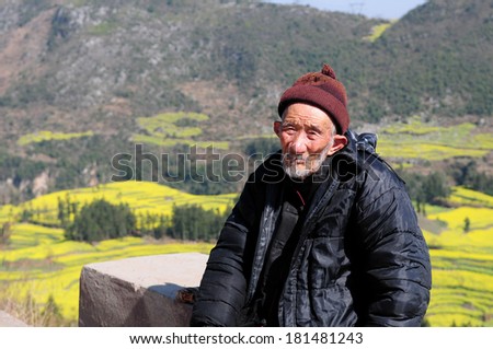 LUOPING, CHINA, FEBRUARY 24: Unidentified old man is near yellow rapeseed field on February 24, 2014 in Luoping, China. Luoping is famous for rapeseed fields