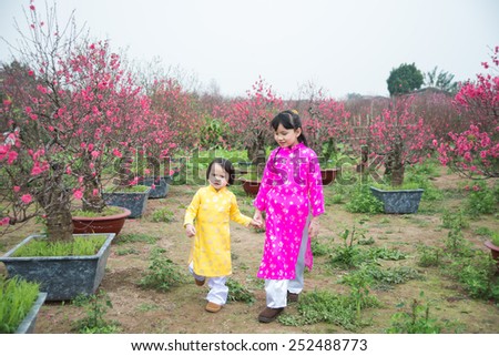 HANOI, VIETNAM, FEB 8: Two kids with traditional dress (ao dai) in peach flower garden on February 8, 2015 in Hanoi, Vietnam. Peach flower is used for decoration in lunar new year in Vietnam.