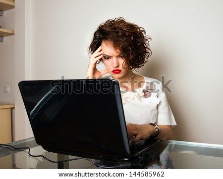Female with curly hair, sitting at desk with hand on head, stressed and worried.