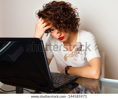 Exhausted woman with curly hair looks at her laptop disappointed