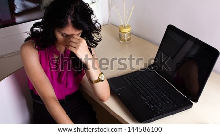 Business woman enduring headaches at her office beside her laptop.