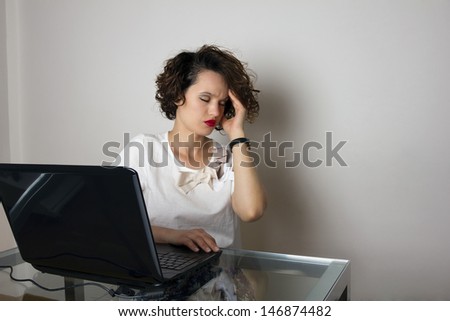 Stressed business woman, working at her desk, with a headache, holding head with left hand, isolated, studio shoot.