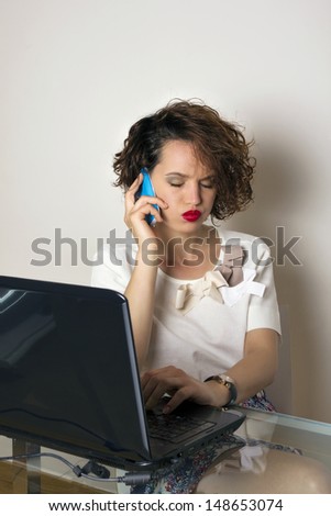 Stressed business woman sitting at her desk, talking on the phone with a desperate gesture, isolated, studio shoot