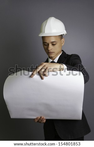 Portrait of a young engineer holding construction plans, analyzing, professional, formal, suit and tie, gray background, studio shoot.