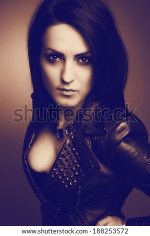 Rock girl, wearing leather jacket, sexy cleavage and eyes fixed on the glass. Vintage portrait.