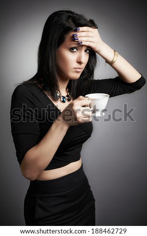 Young lady dressed in a sleek black having a headache, drink hot tea. Gray background.