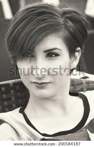 Portrait of a girl with short red hair, sitting on the chair. Black & white picture.