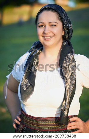 Pretty woman with hands on hips posing in traditional costume and scarf. Romanian folklore.