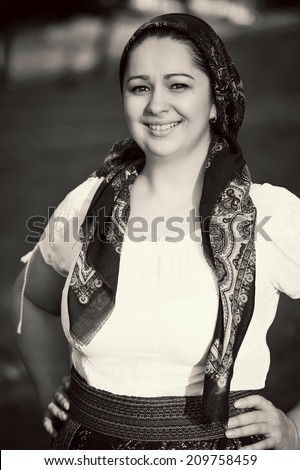 Pretty woman with hands on hips posing in traditional costume and scarf. Romanian folklore. Black and white picture
