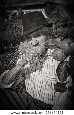 Wrinkled and expressive old farmer leaning on an apple tree in the yard. Black and white picture.