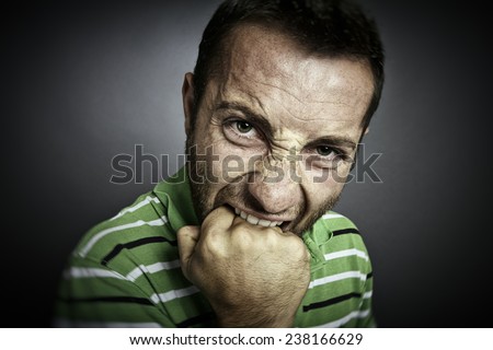 Closeup portrait of an angry guy biting his fist, looking at the camera.