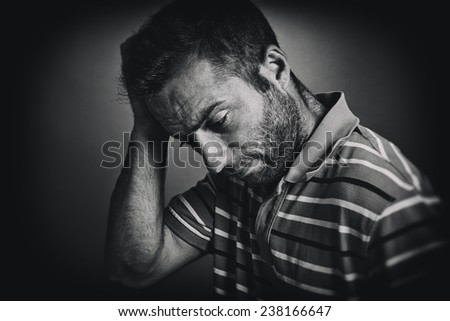 Portrait of thoughtful young man scratching his head, looking down. Black and white style picture.