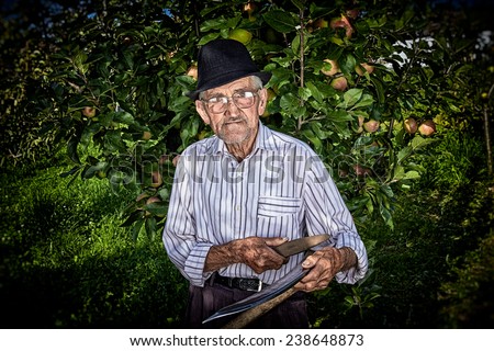 Wrinkled and expressive old farmer sharpening his scythe with an apple tree in the background.