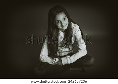 Beautiful little girl sitting with her legs crossed. Gray background. Sepia picture.
