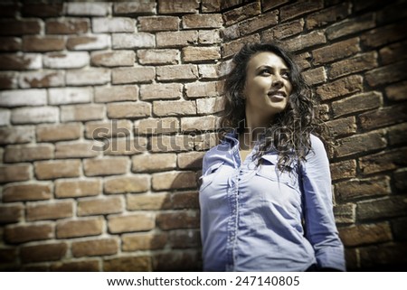 Pretty young city girl standing against an exterior brick wall.